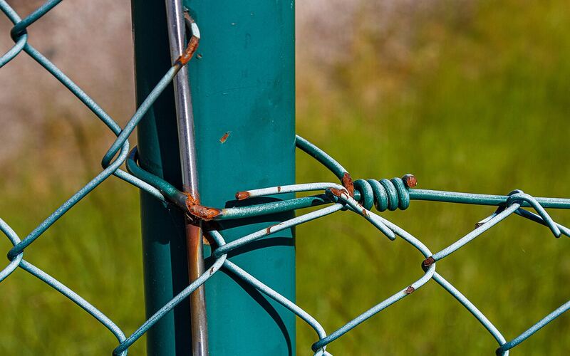 Green PVC-coated chainlink fence mesh tied to a fence post